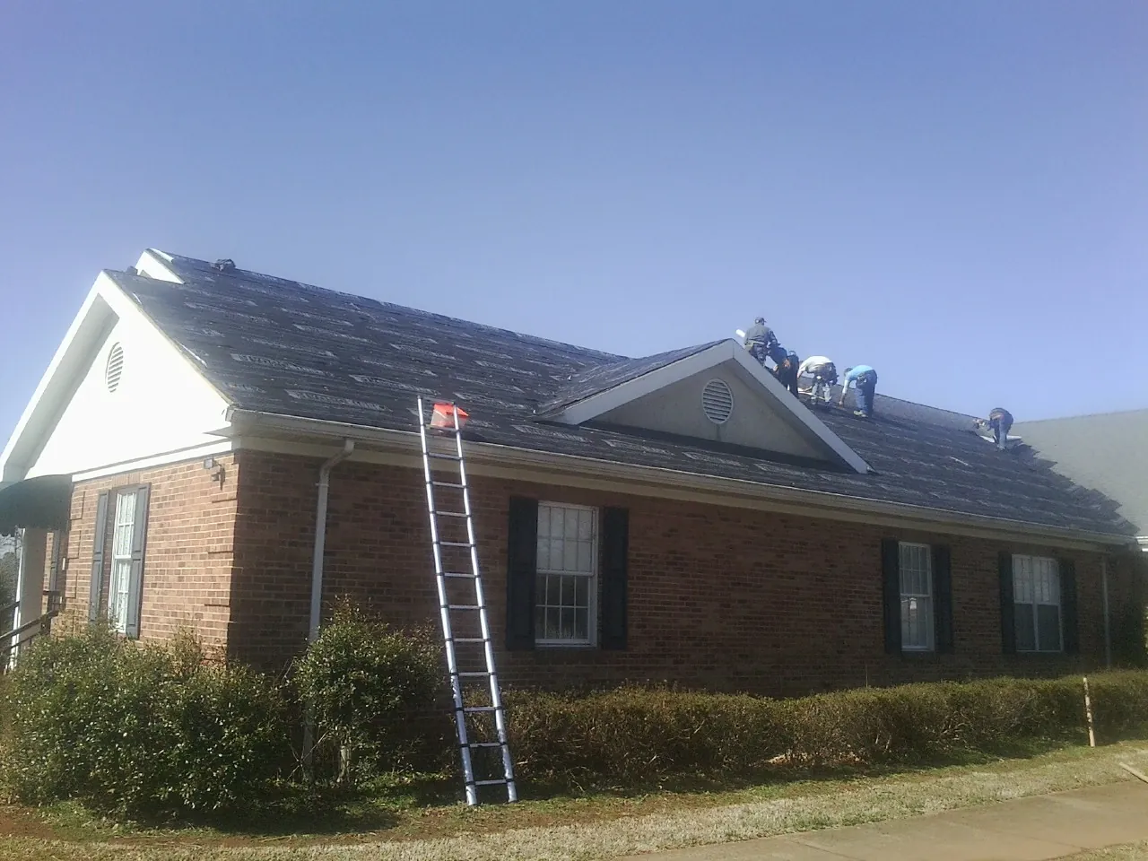 Crew tearing shingles off a brick ranch roof with a ladder set — Metal Roof Repair work by our crew in Sand Springs