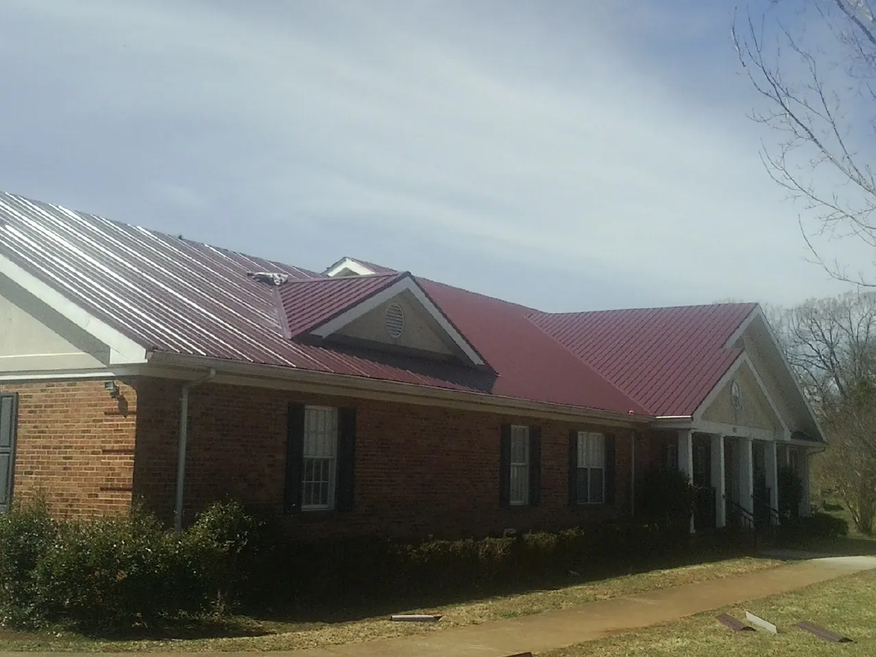 Red metal roof with gabled entries on a long brick building, from a Hail Damage Roof Repair job in Sand Springs
