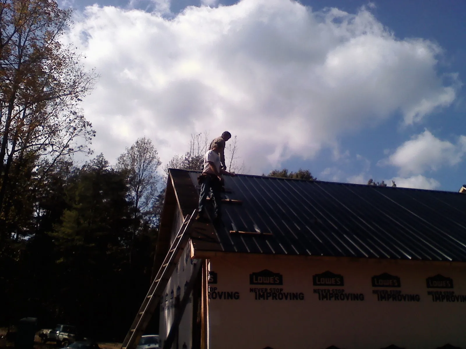 Roofer fastening dark metal panels high against a cloudy sky, from a Roof Inspection job in Sand Springs