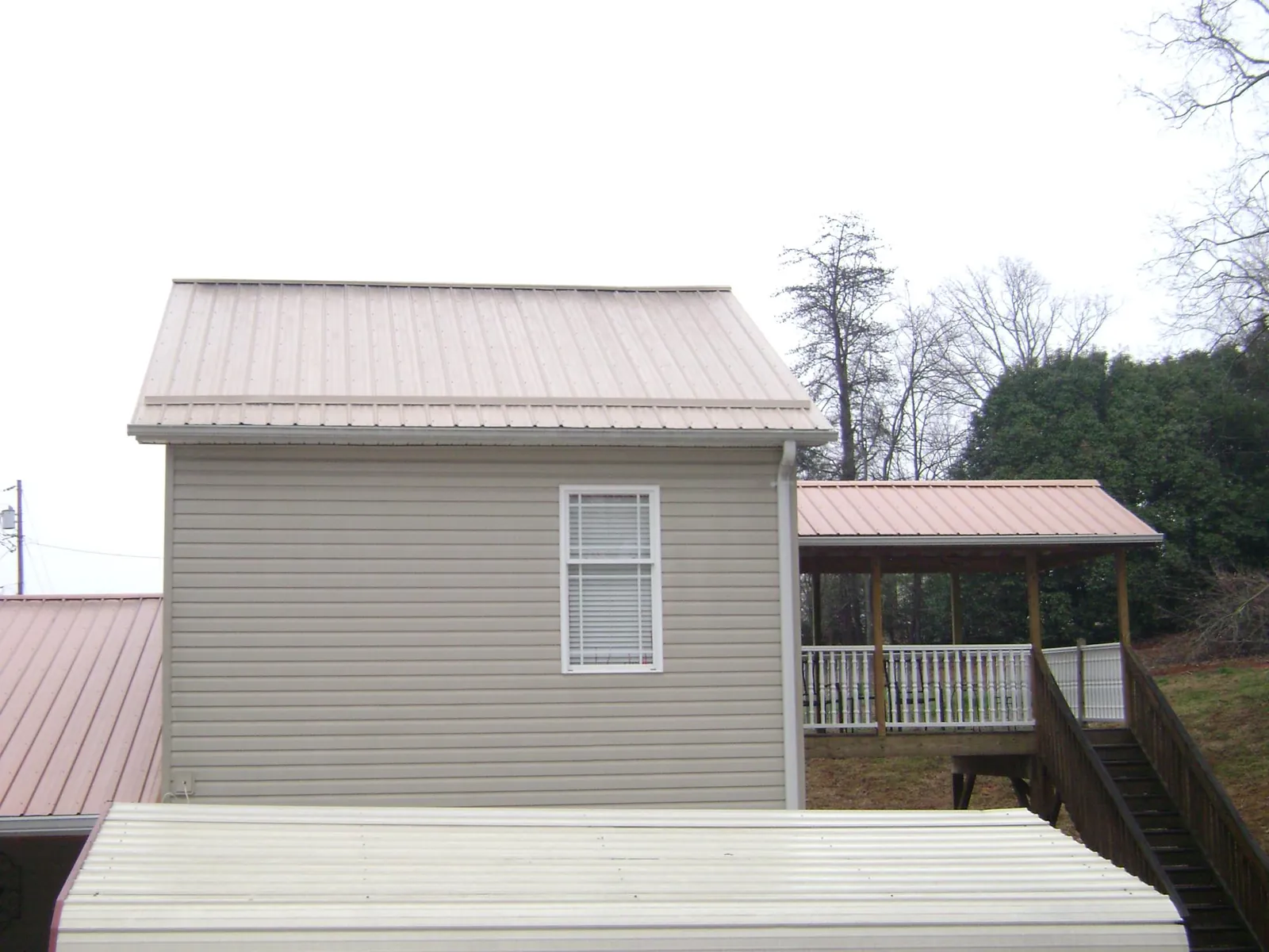 Tan metal roofs on a two story addition and attached porch, from a Roof Replacement job in Sand Springs